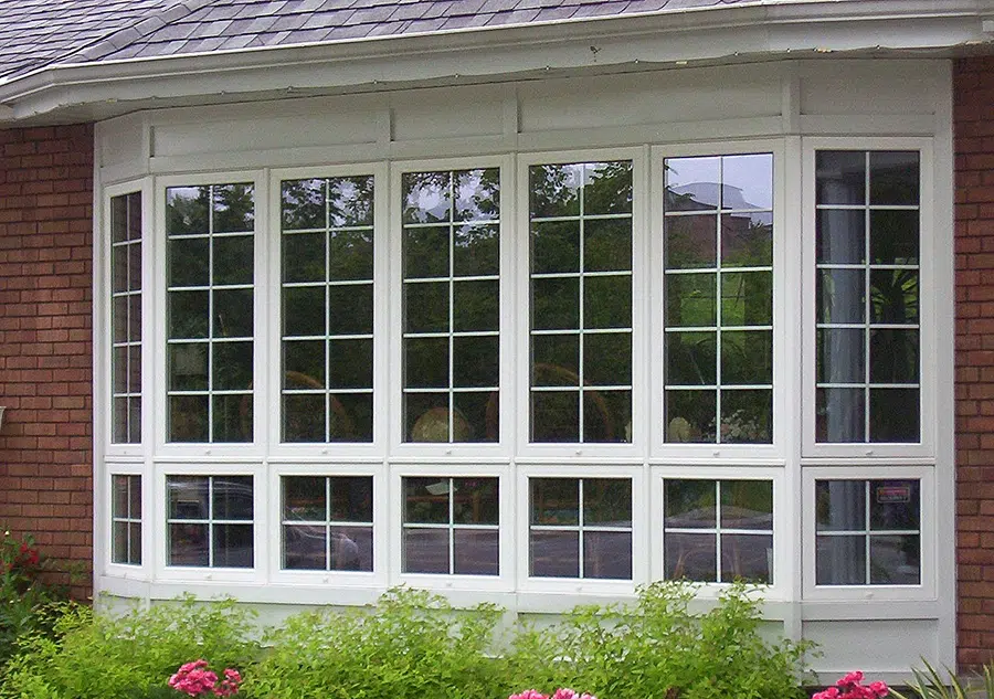 Custom Windows & Doors product image featuring a house with a large window and a colorful flower bed in front.
