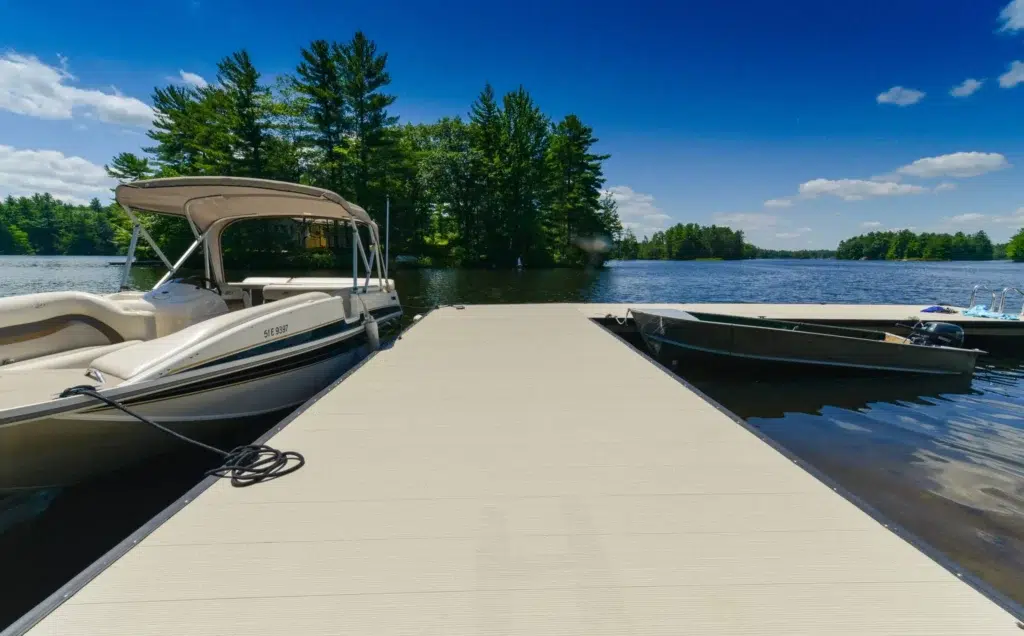 A close-up view of an aluminum deck dock with a pontoon boat and another small boat tied to it, under a bright blue sky.